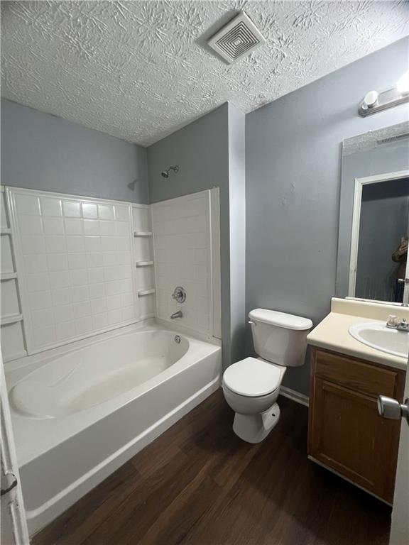 bathroom featuring wood finished floors, toilet, tub / shower combination, vanity, and a textured ceiling