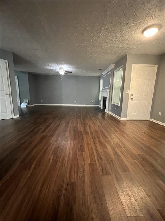 unfurnished living room featuring dark wood-type flooring, baseboards, a fireplace, and a textured ceiling