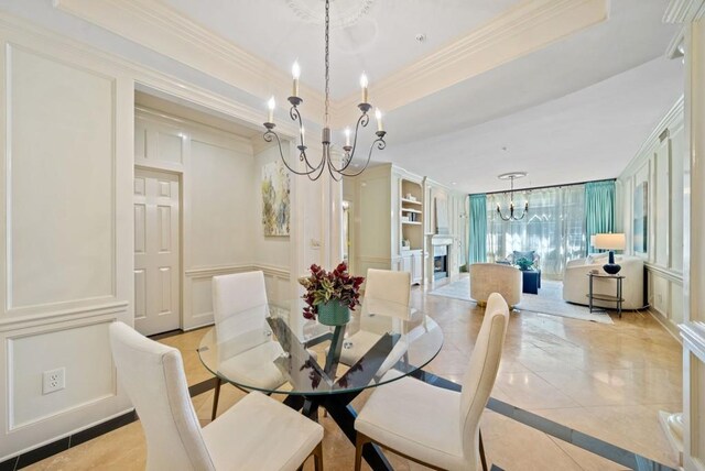 dining room with ornate columns, light tile patterned flooring, ornamental molding, a tray ceiling, and an inviting chandelier