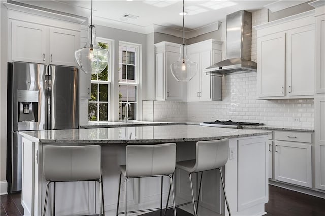 kitchen with white cabinetry, hanging light fixtures, a kitchen island, wall chimney range hood, and appliances with stainless steel finishes