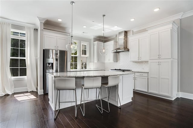 kitchen with white cabinets, decorative light fixtures, a kitchen island, and wall chimney range hood