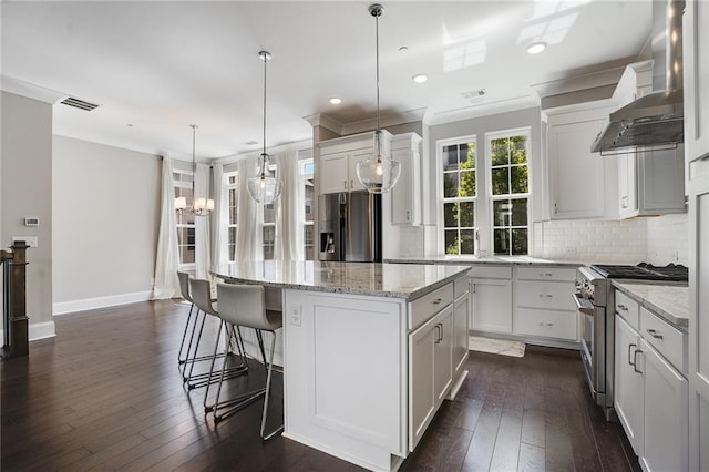 kitchen with white cabinets, a kitchen island, dark hardwood / wood-style flooring, stainless steel appliances, and wall chimney range hood