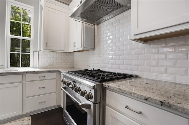 kitchen with high end stove, white cabinets, wall chimney exhaust hood, decorative backsplash, and light stone countertops