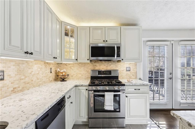 10475 Willow Meadow Cir, Alpharetta, GA 30022 - kitchen with appliances with stainless steel finishes, light stone counters, glass insert cabinets, a textured ceiling, and backsplash