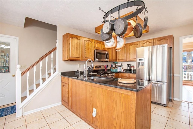 kitchen with light tile patterned flooring, appliances with stainless steel finishes, dark stone countertops, and kitchen peninsula