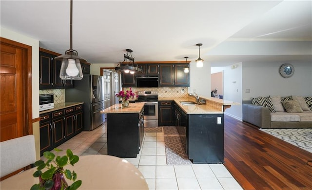 kitchen with kitchen peninsula, stainless steel appliances, sink, a kitchen island, and hanging light fixtures