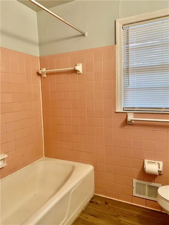 bathroom featuring visible vents, tile walls, toilet, shower / bath combination, and wood finished floors