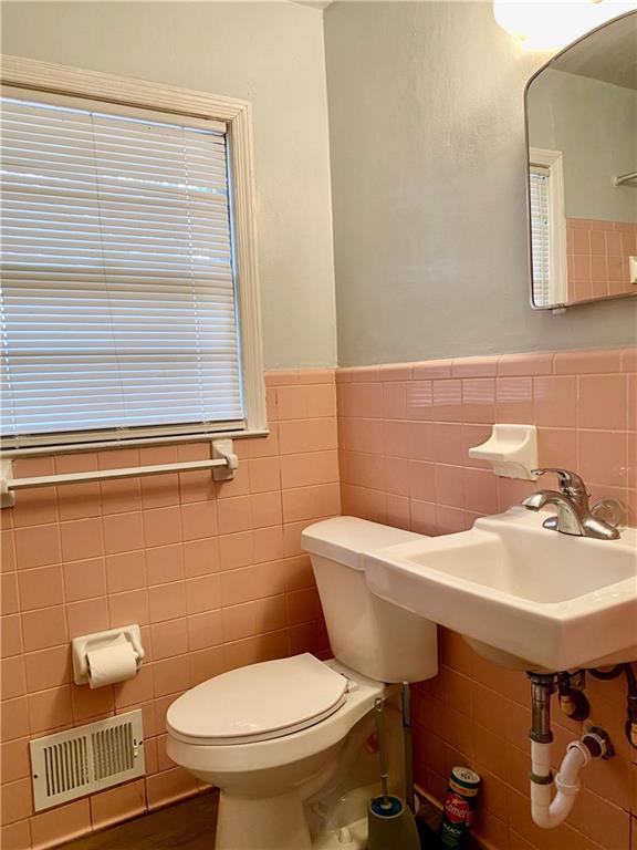bathroom with tile walls, visible vents, a wainscoted wall, and toilet