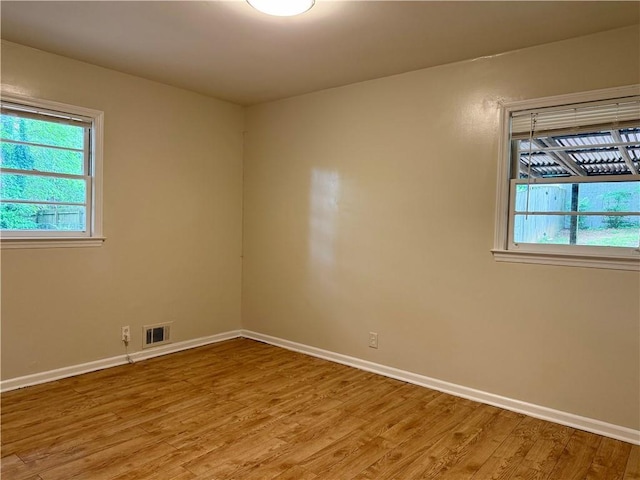 unfurnished room with visible vents, light wood-type flooring, a healthy amount of sunlight, and baseboards