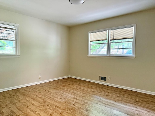 unfurnished room featuring a wealth of natural light, visible vents, wood finished floors, and baseboards