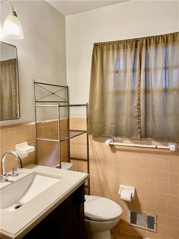 bathroom featuring visible vents, toilet, tile walls, vanity, and wainscoting