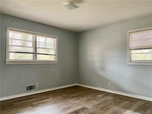 empty room featuring a wealth of natural light, visible vents, and dark wood finished floors