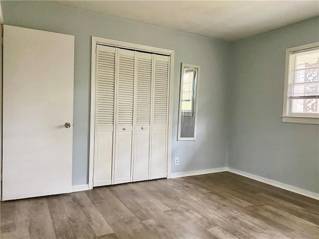 unfurnished bedroom featuring baseboards, wood finished floors, and a closet