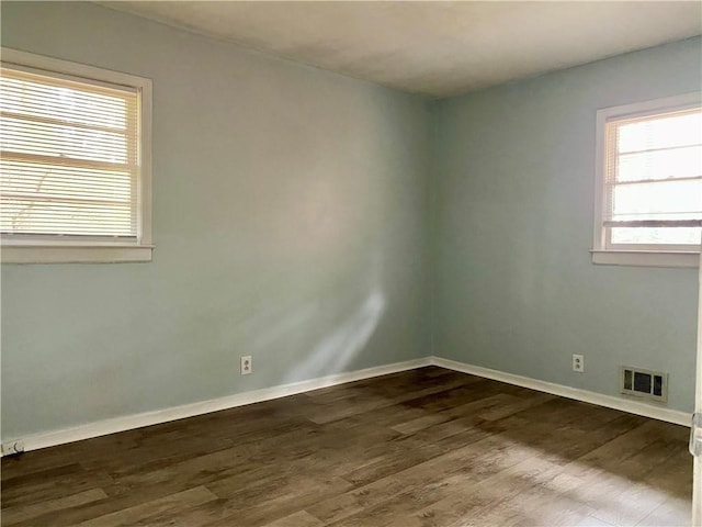 unfurnished room featuring dark wood-style flooring, visible vents, and baseboards