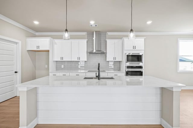 kitchen with stainless steel appliances, white cabinetry, a spacious island, and wall chimney range hood