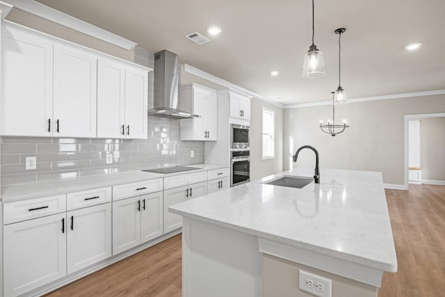 kitchen with stainless steel appliances, a sink, white cabinets, crown molding, and wall chimney range hood