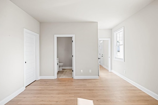 unfurnished bedroom with ensuite bathroom, light wood-type flooring, and baseboards