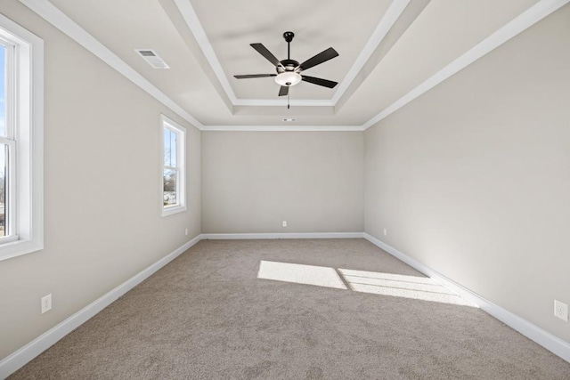 carpeted empty room with visible vents, ceiling fan, baseboards, a tray ceiling, and ornamental molding