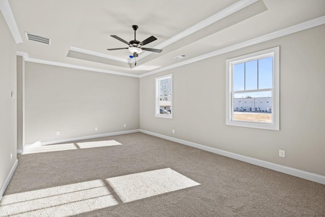 carpeted empty room with visible vents, crown molding, a raised ceiling, and baseboards