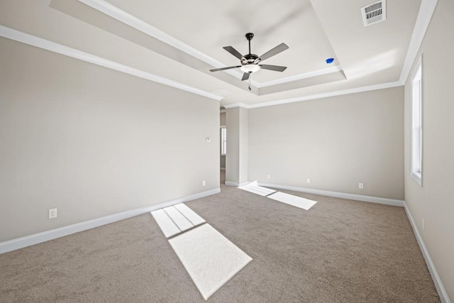 empty room featuring visible vents, ornamental molding, a tray ceiling, carpet floors, and baseboards