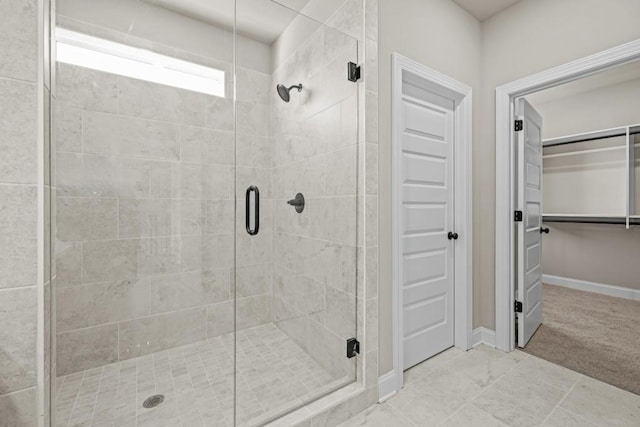 bathroom with a walk in closet, a shower stall, and baseboards