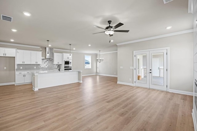 unfurnished living room featuring visible vents, ornamental molding, a sink, ceiling fan with notable chandelier, and light wood-type flooring