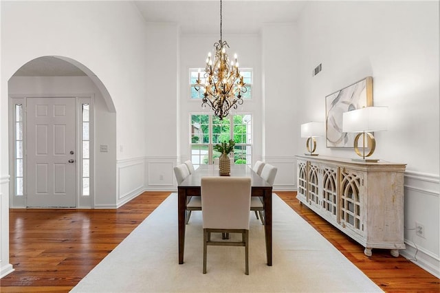 8770 Amberfield Dr, Gainesville, GA 30506 - dining room with arched walkways, a chandelier, wood finished floors, a high ceiling, and wainscoting