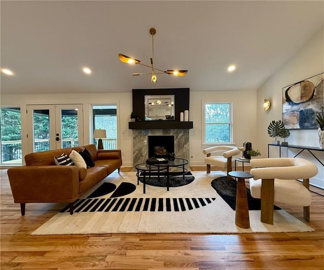 living room with light wood-style floors, vaulted ceiling, a fireplace with raised hearth, and french doors