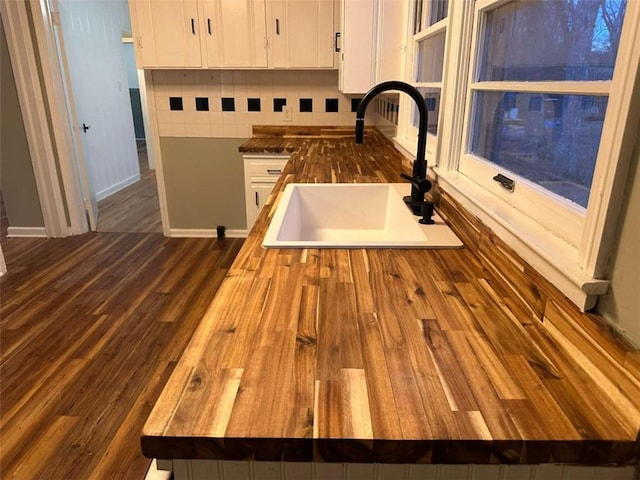 interior details featuring sink, tasteful backsplash, butcher block countertops, dark hardwood / wood-style flooring, and white cabinetry