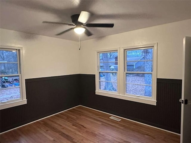 empty room with ceiling fan, wood-type flooring, and wood walls