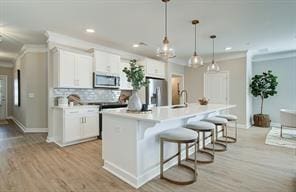 kitchen featuring stainless steel appliances, light countertops, a center island with sink, and light wood-style floors