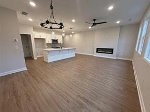 unfurnished living room featuring dark wood-style floors, recessed lighting, a glass covered fireplace, and baseboards