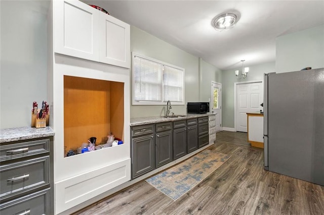 kitchen featuring stainless steel fridge, white cabinetry, light stone countertops, dark wood-type flooring, and sink