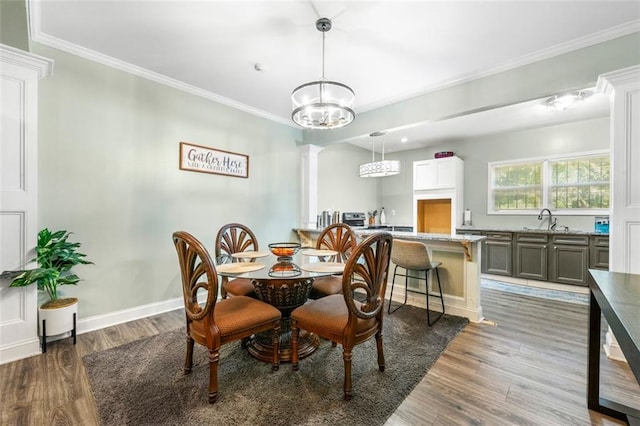 dining room featuring ornamental molding, hardwood / wood-style flooring, sink, and decorative columns