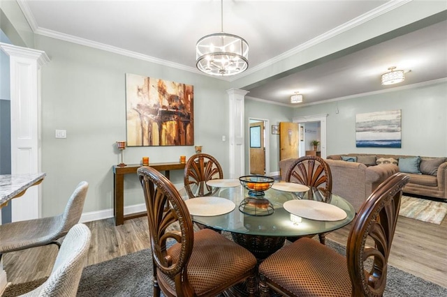 dining room with an inviting chandelier, crown molding, light wood-type flooring, and decorative columns