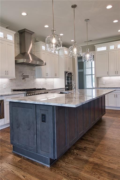 kitchen with a spacious island, dark hardwood / wood-style floors, tasteful backsplash, white cabinetry, and wall chimney range hood