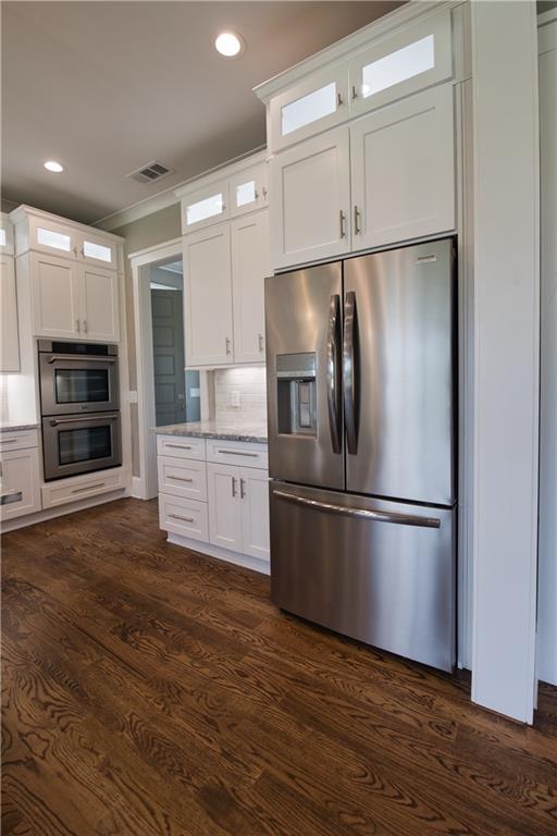 kitchen featuring appliances with stainless steel finishes, dark wood-type flooring, light stone countertops, tasteful backsplash, and white cabinets