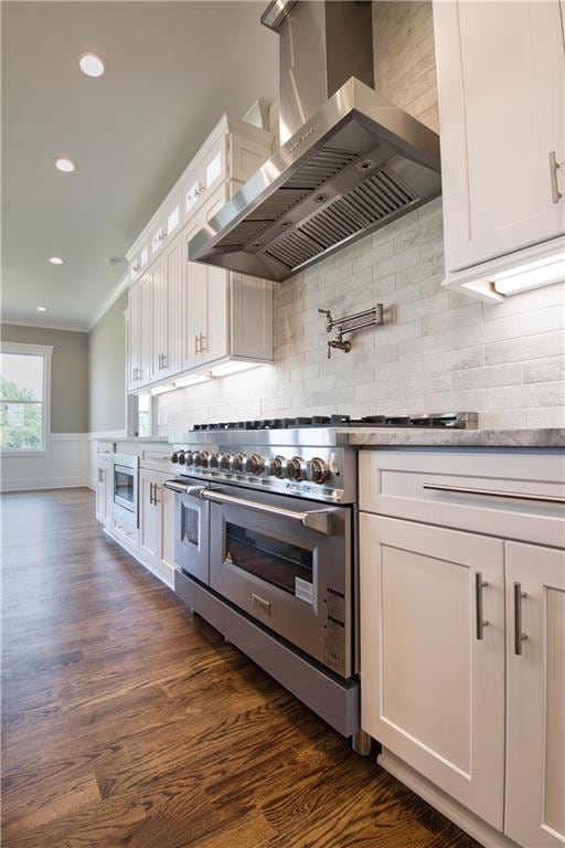 kitchen with wall chimney exhaust hood, dark hardwood / wood-style flooring, tasteful backsplash, ornamental molding, and white cabinetry