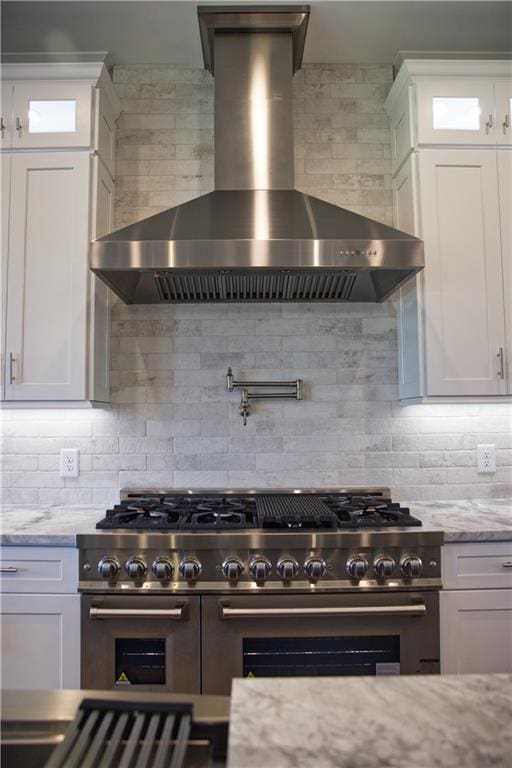 kitchen featuring range with two ovens, wall chimney range hood, tasteful backsplash, and white cabinetry