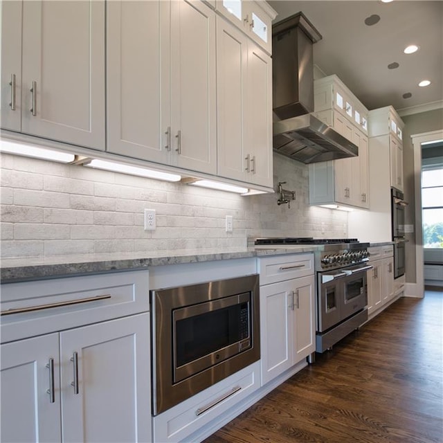 kitchen with stainless steel appliances, decorative backsplash, wall chimney exhaust hood, white cabinets, and dark hardwood / wood-style flooring