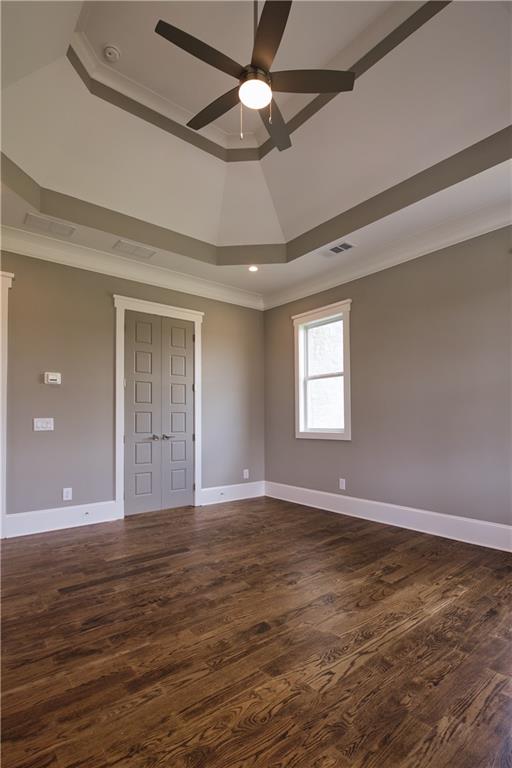 unfurnished bedroom featuring ceiling fan, a raised ceiling, crown molding, and wood-type flooring