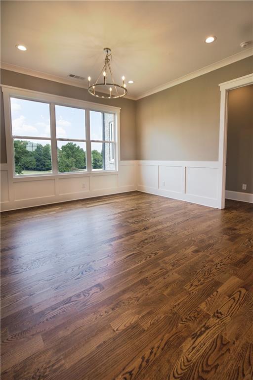 unfurnished room with an inviting chandelier, ornamental molding, and dark hardwood / wood-style flooring