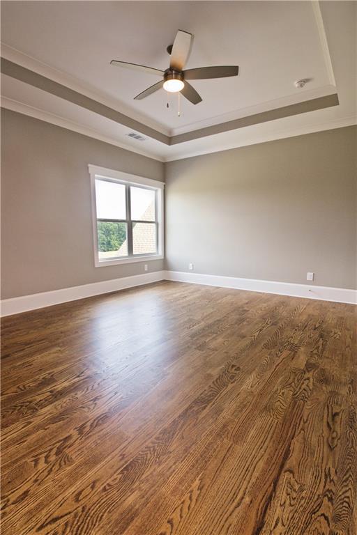 unfurnished room featuring ceiling fan, dark wood-type flooring, ornamental molding, and a tray ceiling