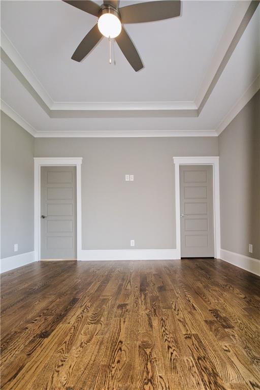 empty room with ceiling fan, a raised ceiling, hardwood / wood-style flooring, and crown molding