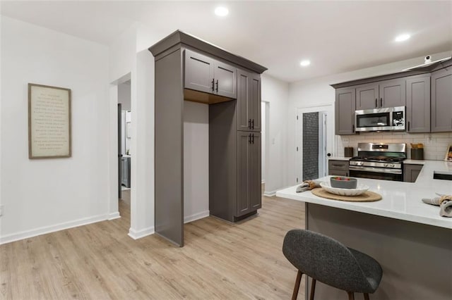 kitchen featuring a breakfast bar, tasteful backsplash, kitchen peninsula, stainless steel appliances, and light wood-type flooring