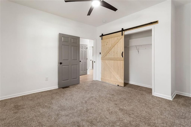 unfurnished bedroom featuring a barn door, carpet floors, ceiling fan, and a closet