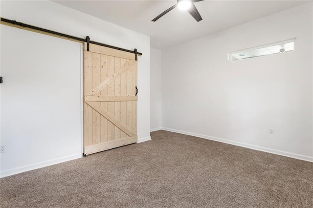 spare room featuring ceiling fan, a barn door, and carpet