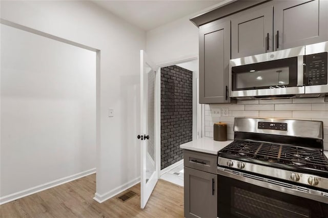 kitchen featuring stainless steel appliances, gray cabinets, light hardwood / wood-style floors, and backsplash