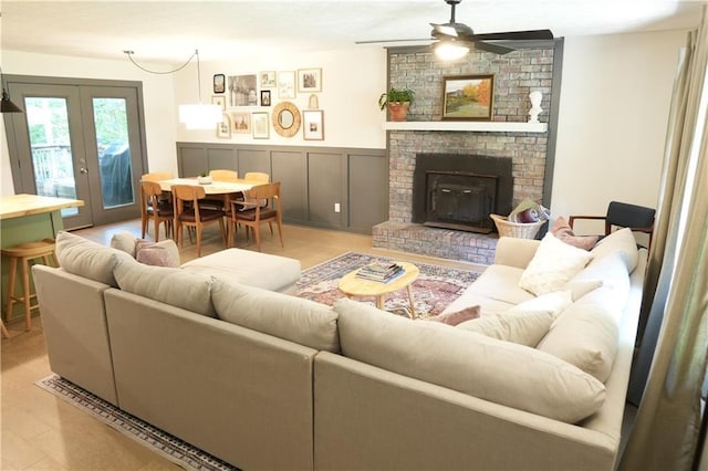 living room featuring ceiling fan, light wood-type flooring, french doors, and a brick fireplace