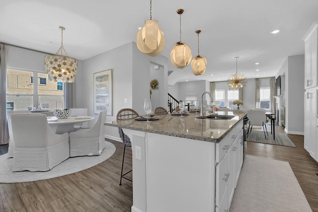 kitchen featuring white cabinets, a sink, an island with sink, wood finished floors, and a kitchen breakfast bar